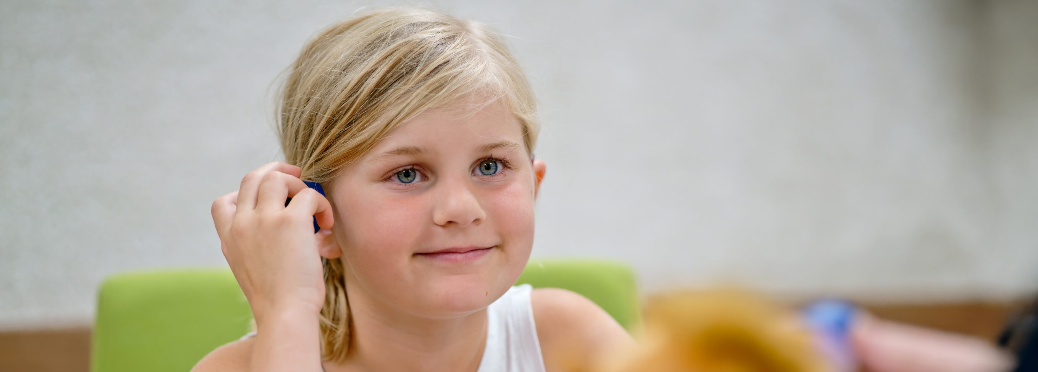 Mädchen setzt sich lächelnd ein Hörgerät ans Ohr – Pädakustik bei Hörgeräte Vogt