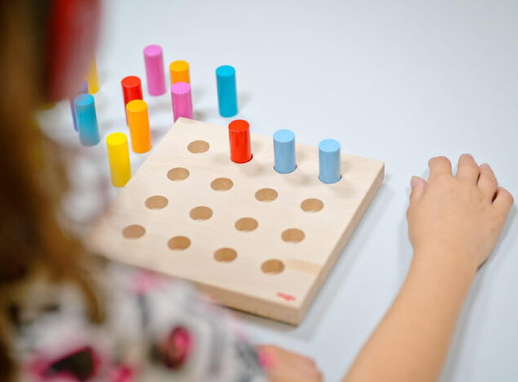 Kind steckt bunte Holzstäbe in ein Steckbrett – spielerische Hörmessung in der Pädakustik